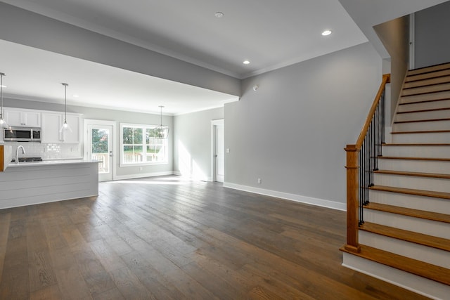 unfurnished living room with recessed lighting, baseboards, ornamental molding, stairway, and dark wood-style floors