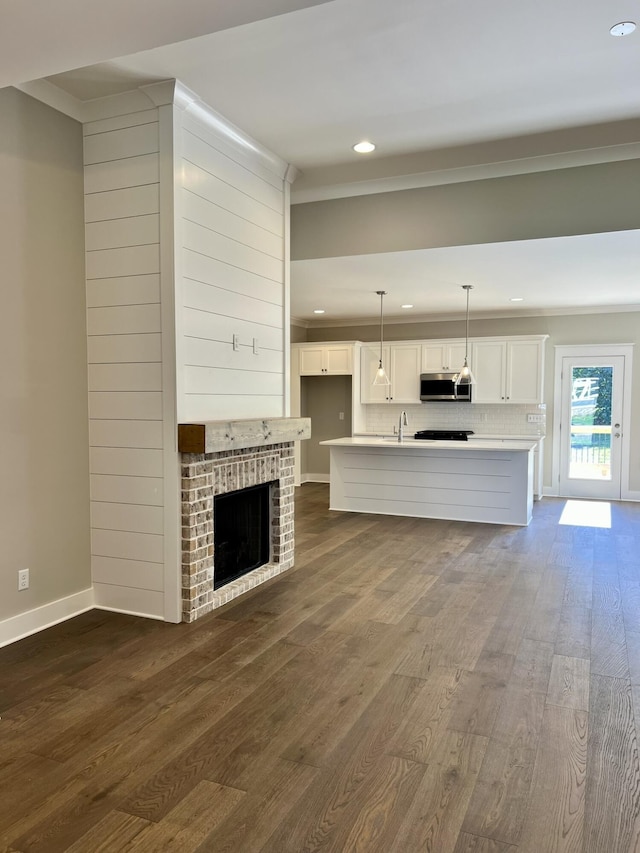 unfurnished living room with recessed lighting, wood finished floors, baseboards, a brick fireplace, and crown molding