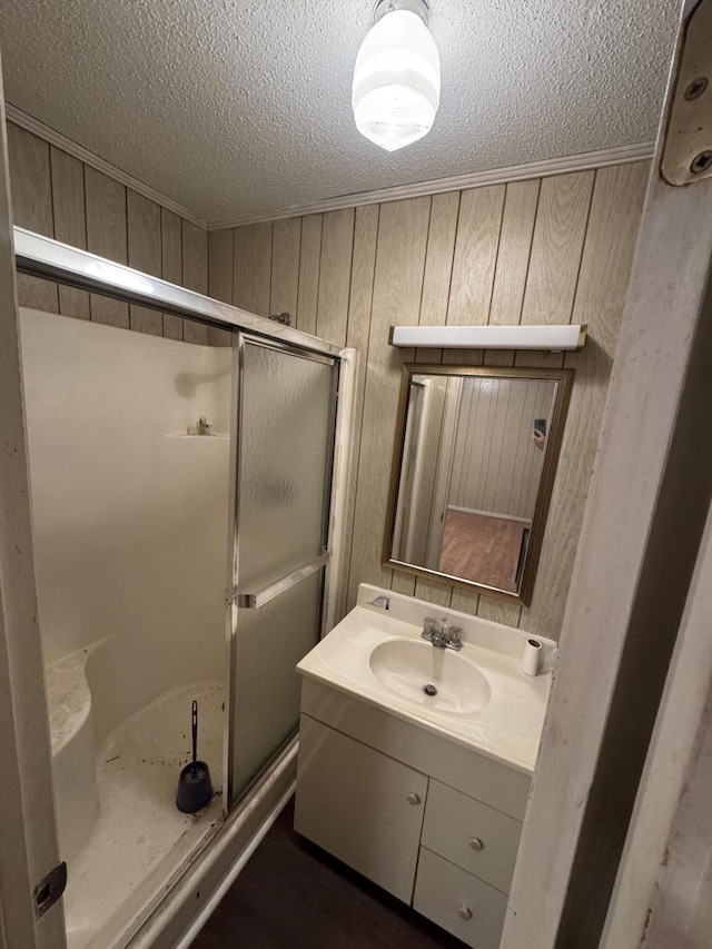 bathroom featuring vanity, a shower with door, wooden walls, and a textured ceiling