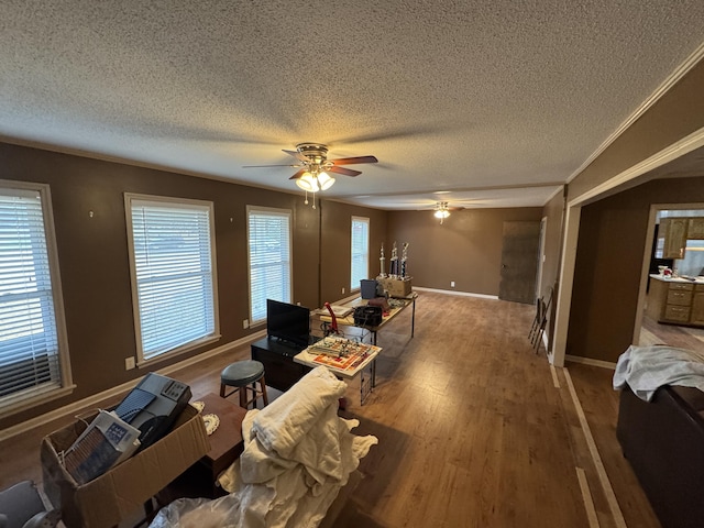 living room with a textured ceiling, ceiling fan, crown molding, and wood-type flooring