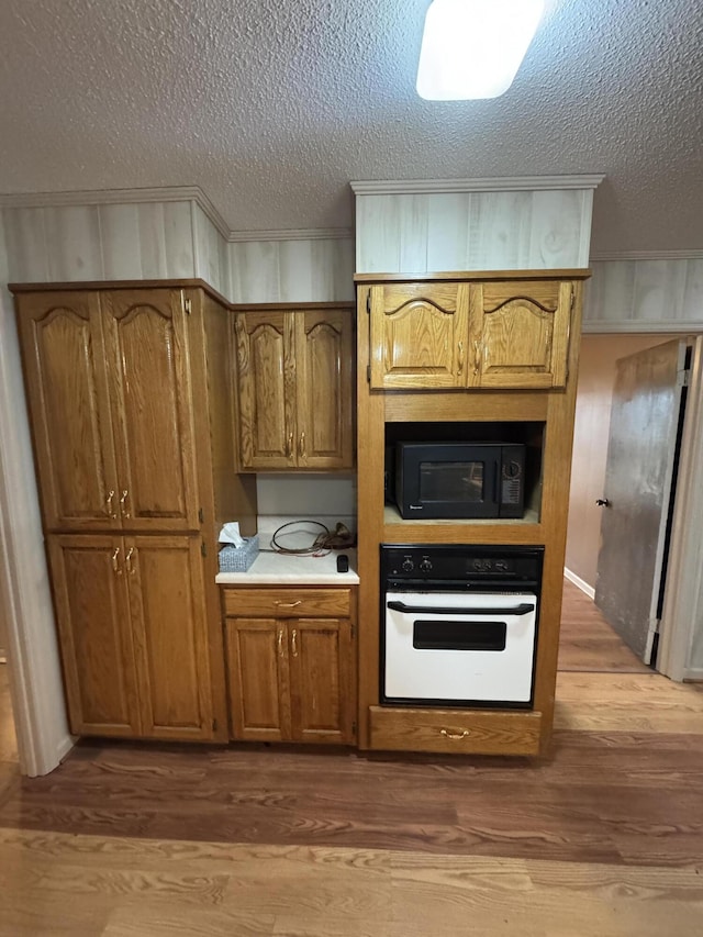 kitchen with white oven, wood walls, a textured ceiling, and hardwood / wood-style flooring