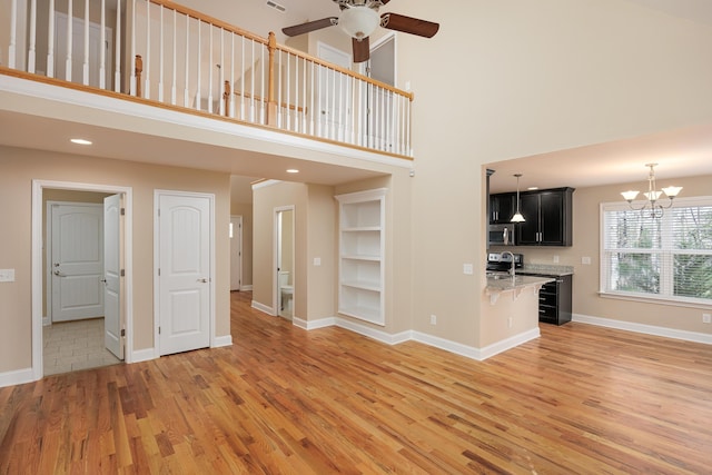 unfurnished living room with ceiling fan with notable chandelier, wood-type flooring, sink, and a high ceiling