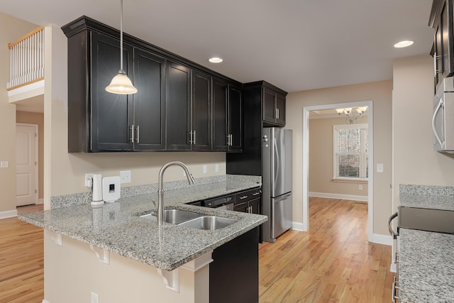 kitchen featuring light stone countertops, sink, light hardwood / wood-style flooring, decorative light fixtures, and a kitchen bar