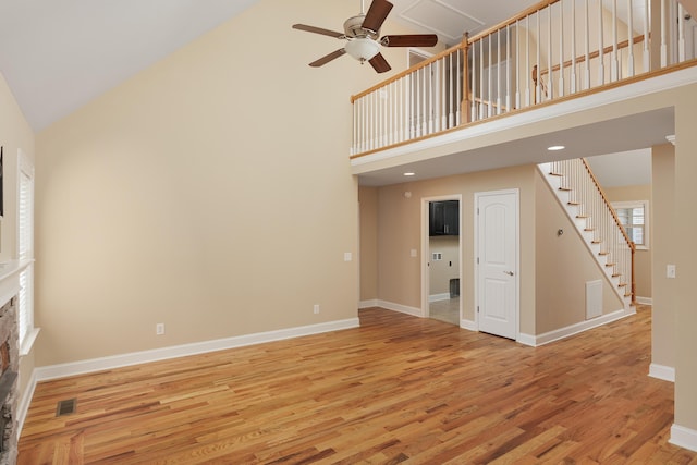 unfurnished living room with ceiling fan, a stone fireplace, light wood-type flooring, and high vaulted ceiling