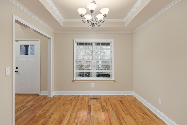 interior space with a tray ceiling, crown molding, a chandelier, and light wood-type flooring