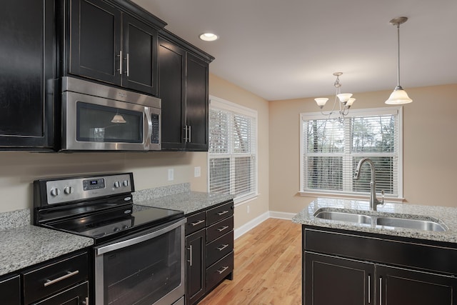 kitchen with pendant lighting, sink, light wood-type flooring, appliances with stainless steel finishes, and a notable chandelier