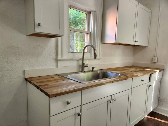 kitchen with butcher block countertops, white cabinets, and sink