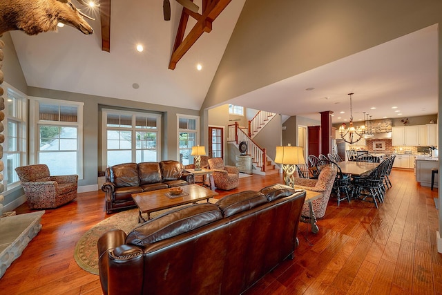 living area featuring wood-type flooring, an inviting chandelier, stairs, high vaulted ceiling, and beam ceiling