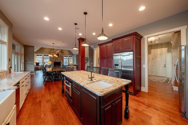 kitchen with lofted ceiling, stainless steel appliances, hanging light fixtures, and light wood-type flooring