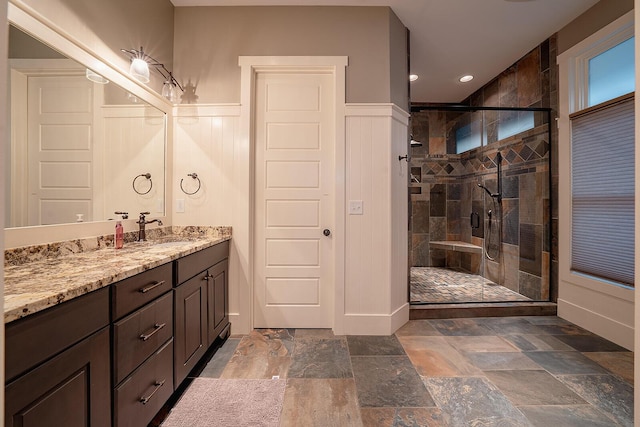 bathroom featuring recessed lighting, vanity, wainscoting, stone finish flooring, and a stall shower