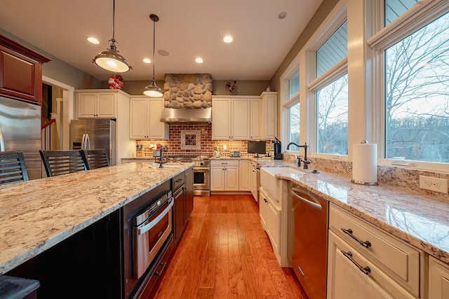 kitchen with light stone counters, a sink, high quality appliances, light wood-type flooring, and pendant lighting