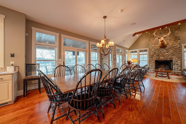 dining room with a notable chandelier, light wood-style floors, a stone fireplace, high vaulted ceiling, and baseboards