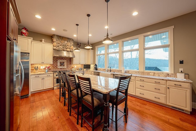 kitchen featuring tasteful backsplash, custom range hood, light stone countertops, light wood finished floors, and pendant lighting