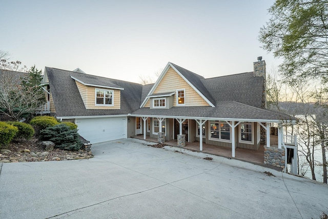 view of front facade with a porch, concrete driveway, roof with shingles, board and batten siding, and a chimney