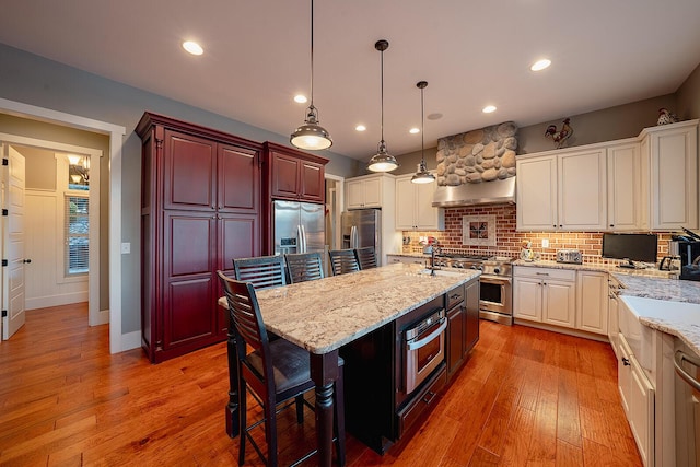 kitchen with light stone counters, pendant lighting, stainless steel appliances, tasteful backsplash, and light wood-type flooring