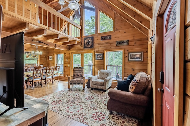 living room with wood ceiling, ceiling fan with notable chandelier, wooden walls, high vaulted ceiling, and light hardwood / wood-style flooring