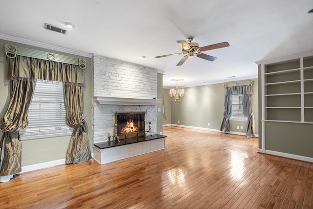 unfurnished living room featuring hardwood / wood-style flooring, ceiling fan with notable chandelier, a stone fireplace, and crown molding