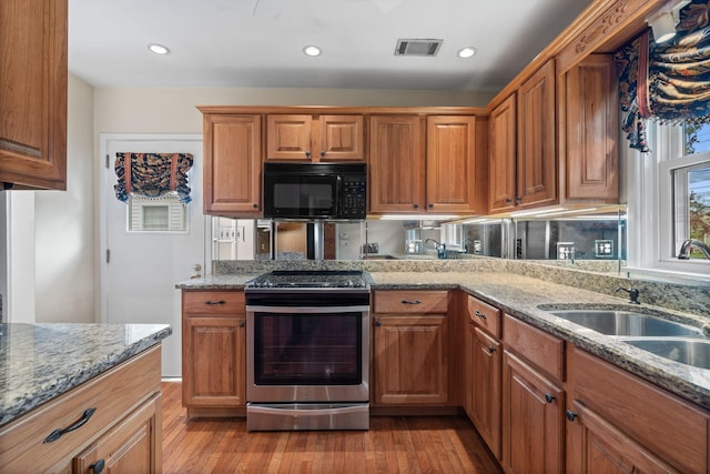 kitchen with stainless steel electric range oven, light hardwood / wood-style flooring, light stone countertops, and sink