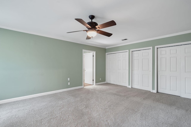 unfurnished bedroom with carpet, multiple closets, ceiling fan, and ornamental molding