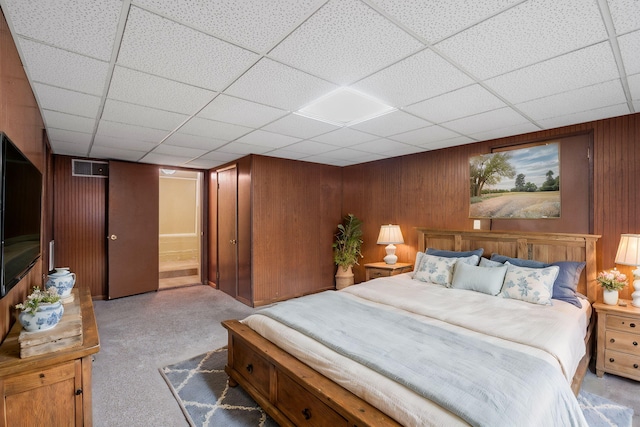 carpeted bedroom with a paneled ceiling and wood walls