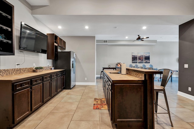 kitchen with butcher block counters, sink, stainless steel fridge with ice dispenser, an island with sink, and a breakfast bar area