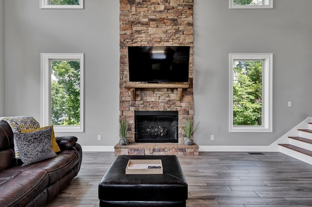 living room featuring a towering ceiling, a stone fireplace, and dark wood-type flooring