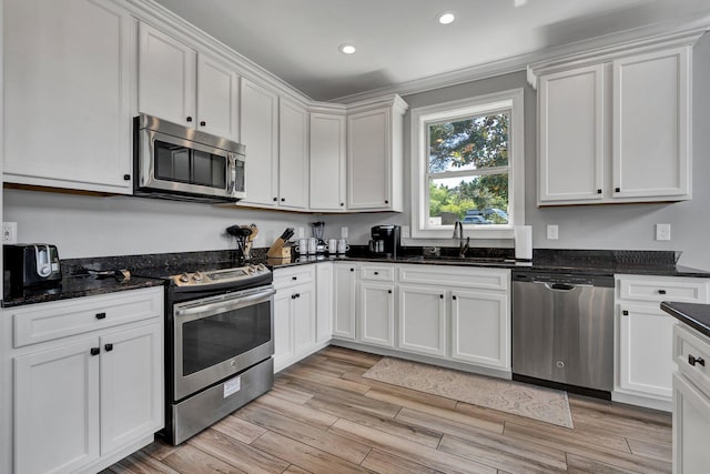 kitchen featuring sink, dark stone countertops, appliances with stainless steel finishes, white cabinets, and light wood-type flooring