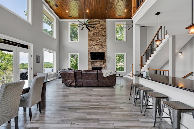 living room featuring a wealth of natural light, a high ceiling, a stone fireplace, light hardwood / wood-style flooring, and wood ceiling