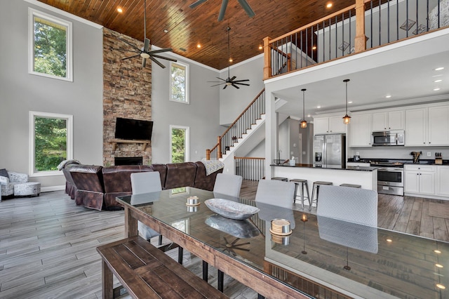 dining room with a stone fireplace, light hardwood / wood-style flooring, high vaulted ceiling, crown molding, and wood ceiling