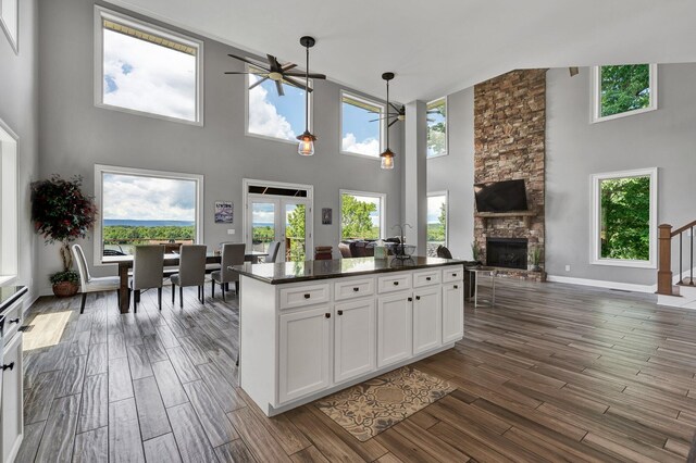 kitchen with white cabinets, ceiling fan, a stone fireplace, and a towering ceiling