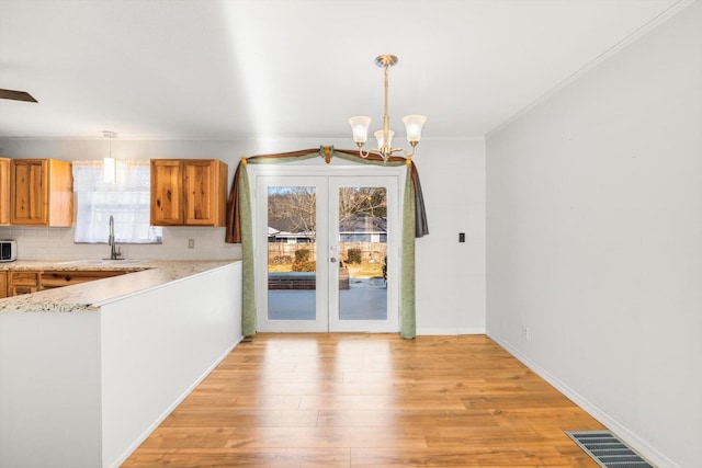 unfurnished dining area featuring french doors, sink, ornamental molding, a notable chandelier, and light wood-type flooring