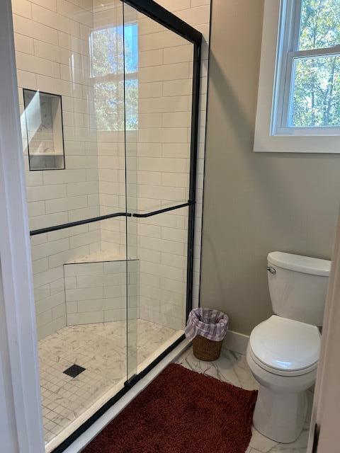 bathroom featuring a shower with door and toilet