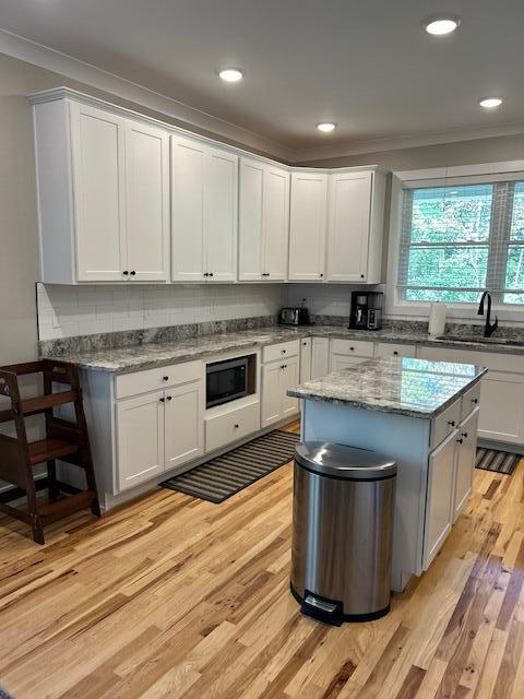 kitchen featuring white cabinets, sink, light stone countertops, light hardwood / wood-style floors, and black microwave