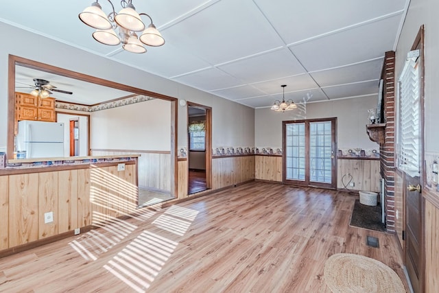 unfurnished dining area with a wainscoted wall, ceiling fan with notable chandelier, wood finished floors, and visible vents