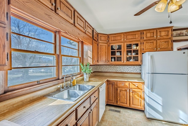 kitchen featuring light countertops, visible vents, brown cabinetry, a sink, and white appliances