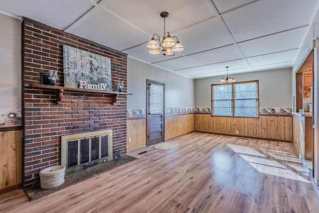 unfurnished living room with wooden walls, a wainscoted wall, wood finished floors, a fireplace, and a chandelier