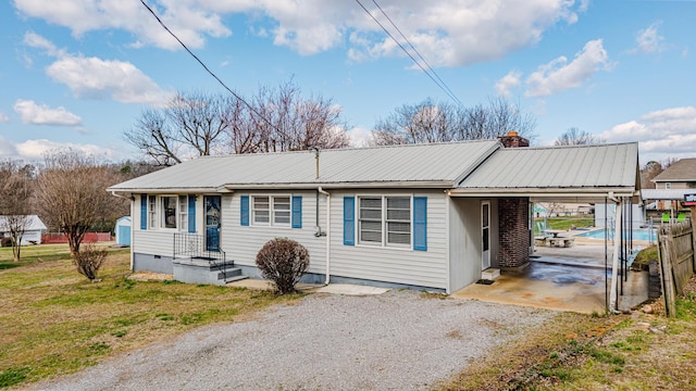 ranch-style house with a chimney, a front yard, metal roof, an attached carport, and driveway