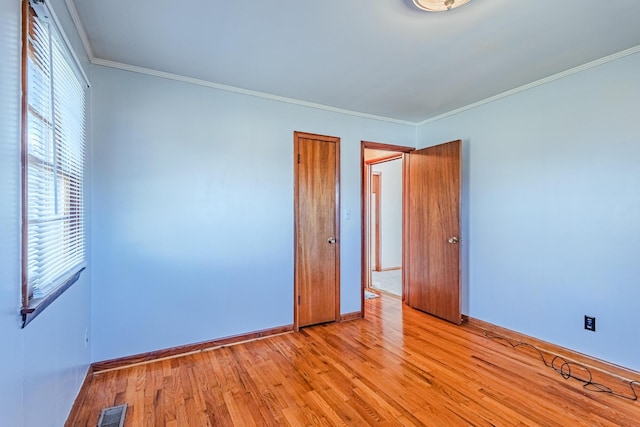 spare room featuring light wood-type flooring, visible vents, crown molding, and baseboards