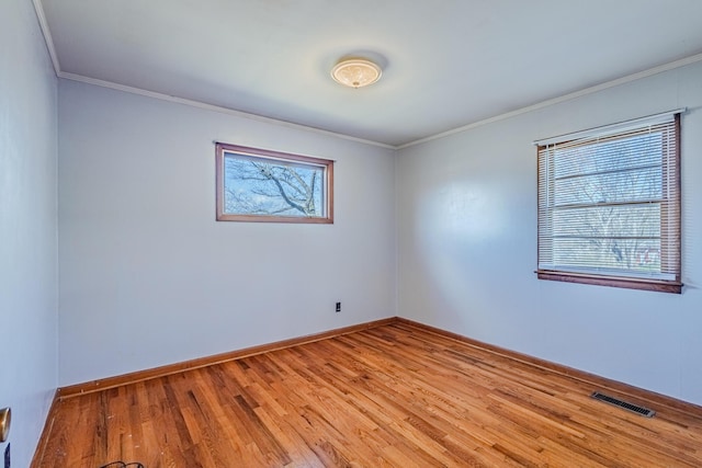 spare room featuring baseboards, visible vents, wood finished floors, and ornamental molding