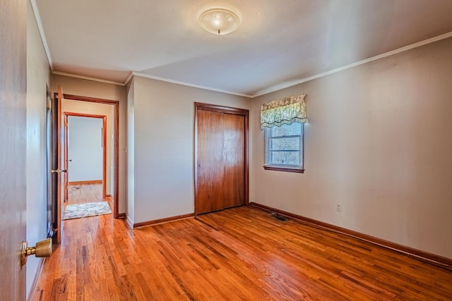 unfurnished bedroom with light wood finished floors, crown molding, baseboards, and a closet