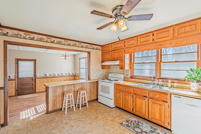 kitchen featuring white appliances, wainscoting, a peninsula, under cabinet range hood, and a sink