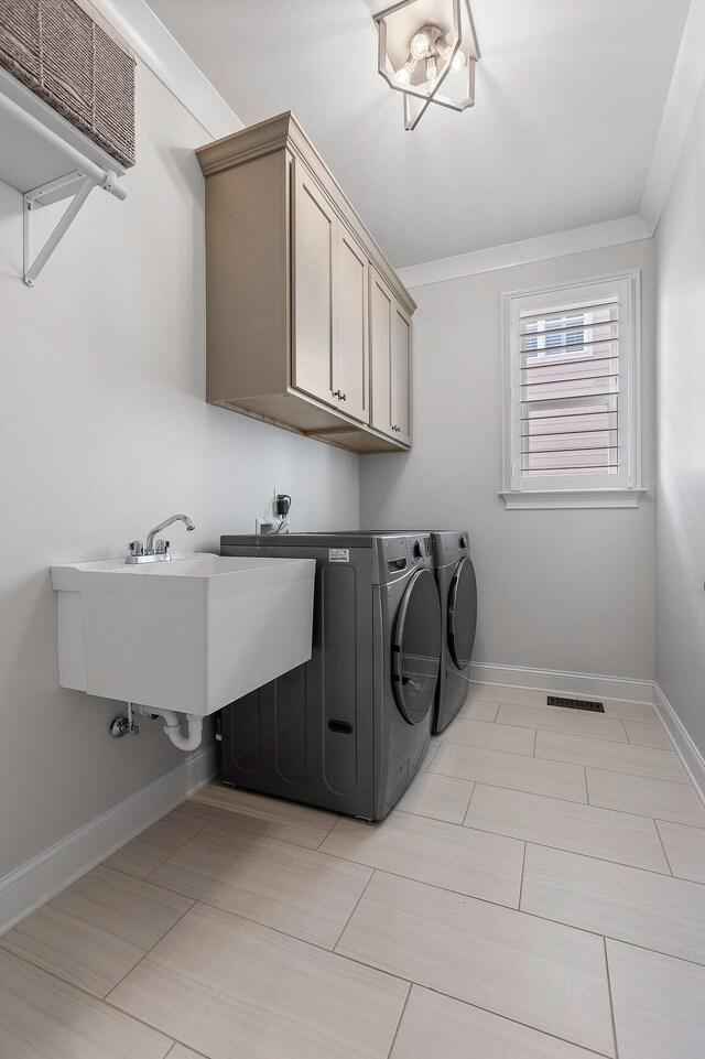 laundry area featuring cabinets, sink, ornamental molding, and washing machine and clothes dryer