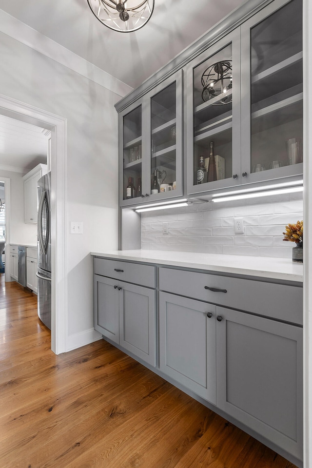 bar featuring appliances with stainless steel finishes, backsplash, gray cabinets, and hardwood / wood-style flooring