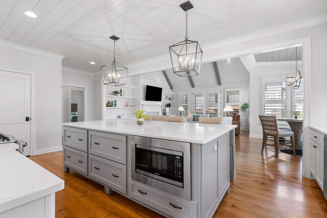 kitchen with pendant lighting, a center island, stainless steel microwave, lofted ceiling with beams, and light hardwood / wood-style floors