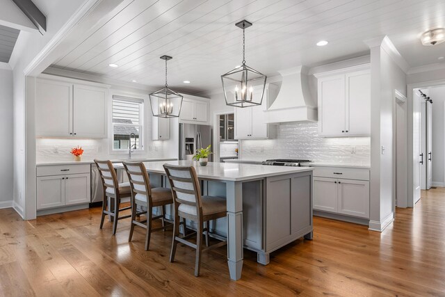 kitchen with a large island, hanging light fixtures, stainless steel appliances, premium range hood, and light hardwood / wood-style floors