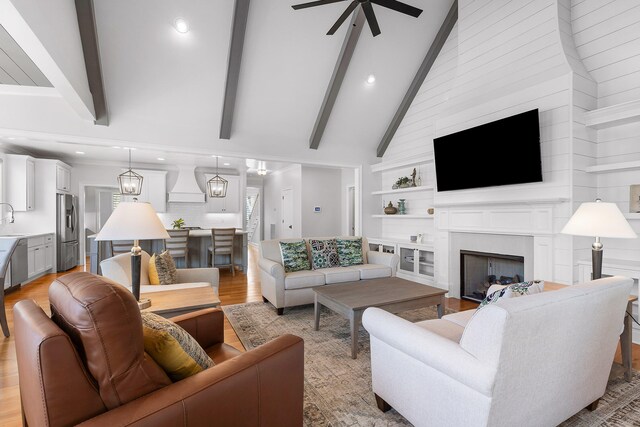 living room featuring high vaulted ceiling, ceiling fan with notable chandelier, sink, light hardwood / wood-style flooring, and beamed ceiling