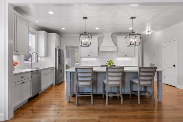 kitchen featuring sink, hanging light fixtures, stainless steel appliances, a kitchen island, and custom exhaust hood