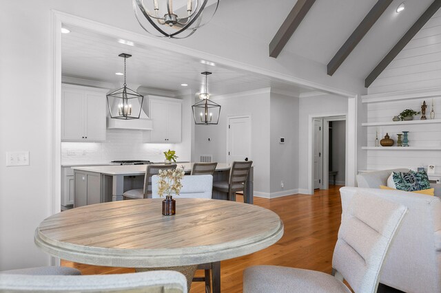 dining space with wood-type flooring, vaulted ceiling with beams, and ornamental molding