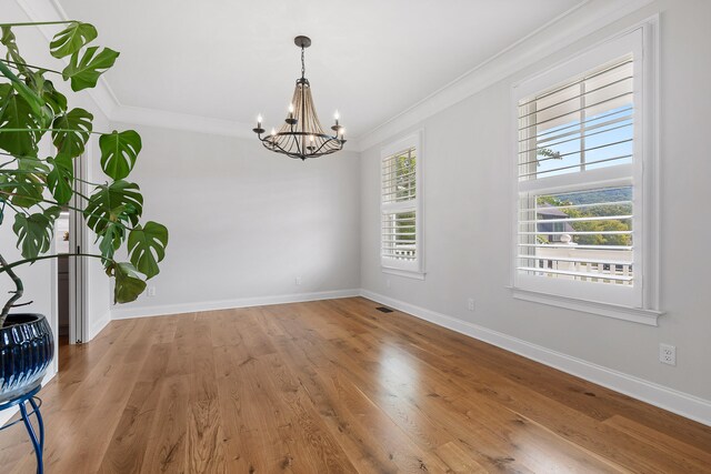 unfurnished dining area featuring hardwood / wood-style flooring, crown molding, and an inviting chandelier