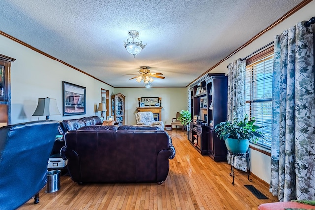 living room with ornamental molding, a textured ceiling, ceiling fan, and light wood-type flooring